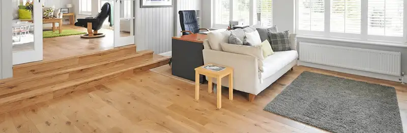 A modern living room with professionally installed laminate flooring, a beige sofa, a small side table, a gray rug, and large windows with white shutters in Fresno, CA